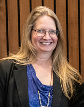 Smiling woman with long hair, wearing glasses and a blue top.