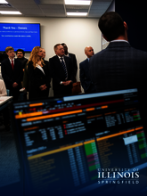 People in business attire attending a presentation, with financial data on screens.