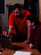 Two men discussing something on a laptop, one pointing at the screen.