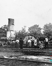 People standing near a tall, damaged building with trees in the background.