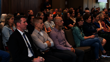 Audience attentively listening in a dimly lit conference room.