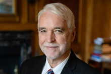 University of Illinois System President Tim Killeen in a suit smiling in a dimly lit room.