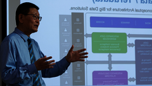 Man giving a presentation with a slide in the background.
