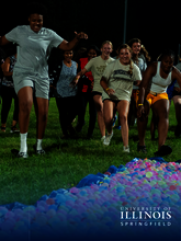 Students running towards colorful balls on a grass field at night.