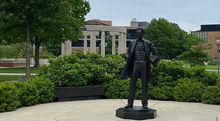 Statue of Abraham Lincoln standing in a garden area with the Colonnade and campus buildings behind.