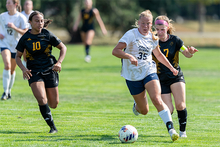 UIS soccer players in action on a green field, one leading with the ball.