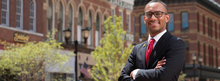 Professional person in a suit smiling, standing with arms crossed in a historic street.