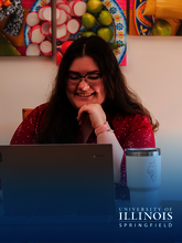 Smiling person with glasses using a laptop, artwork in the background.