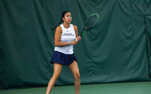 Cristina Mendoza Romero playing tennis indoors in white and blue UIS uniform