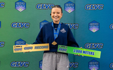 Madelyn Miller Ross poses in front of GLVC branded signage with All-GLVC medal and sign