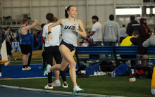 Madelyn Miller-Ross running indoor track in white UIS uniform
