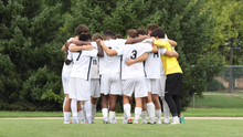 Men's Soccer Huddle on field pre-game, UIS players in white and yellow jerseys