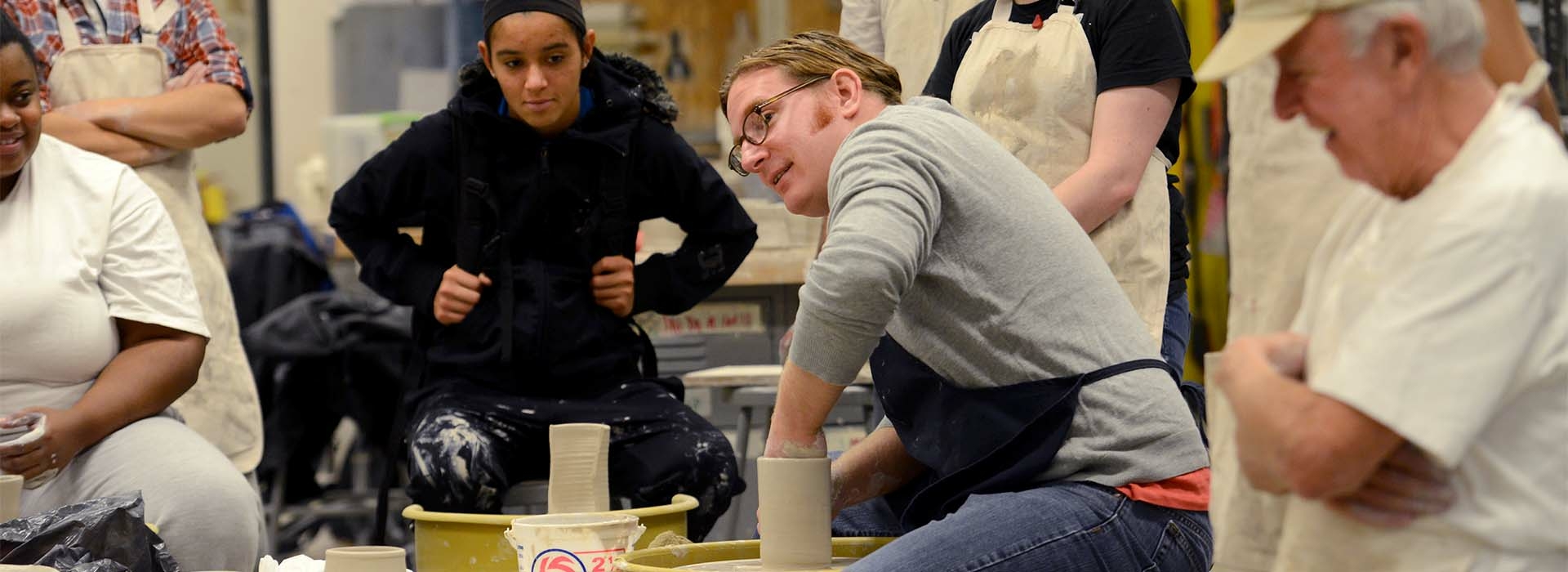 Art faculty member throwing on a ceramics wheel while students watch.