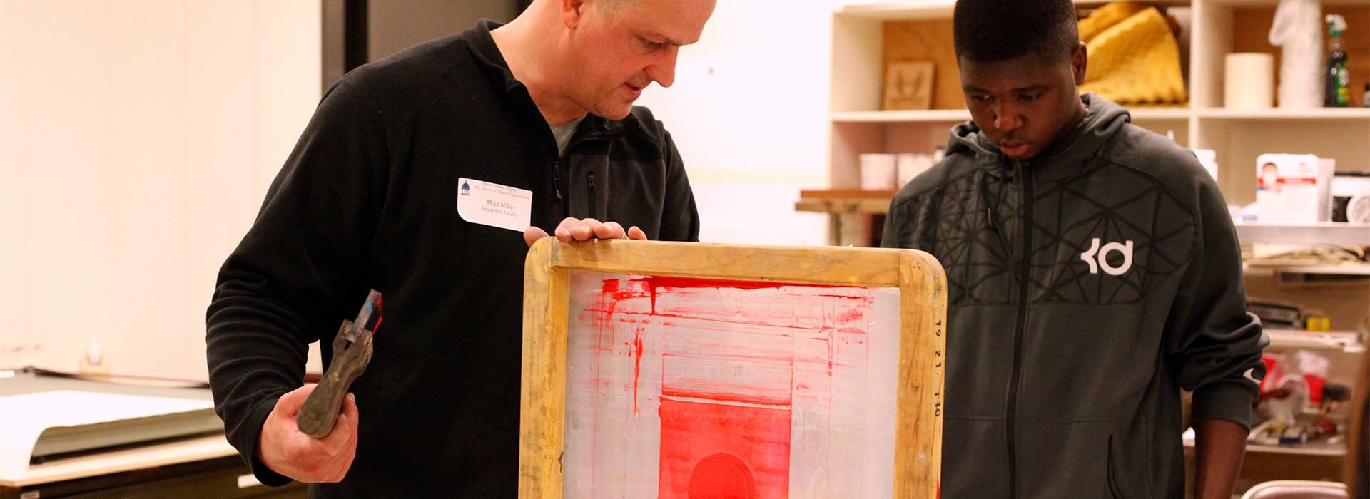 Two men standing over a screen-printing screen.