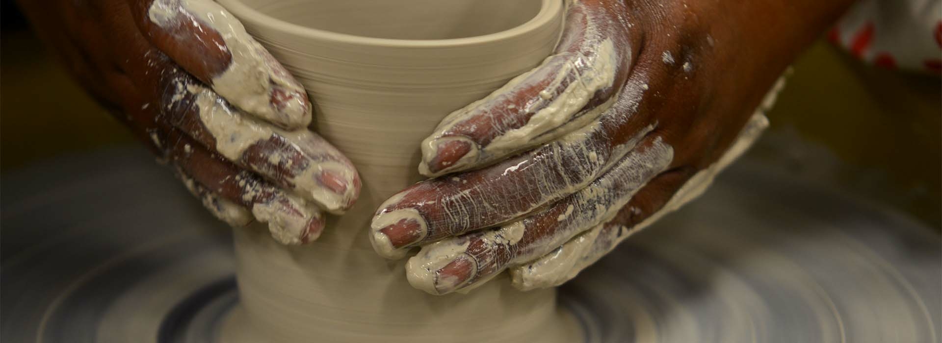 Hands throwing a pot on a ceramics wheel.