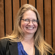 Smiling woman with long hair, wearing glasses and a blue top.