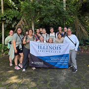 Group of people holding a University of Illinois Springfield banner in a lush, green setting.