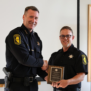 Two uniformed officers smiling as one receives a plaque.