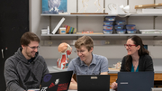 Three people smiling, working on laptops in a lab setting.