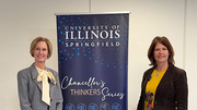 Two women standing beside University of Illinois Springfield banner indoors.