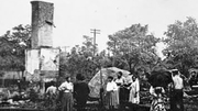 People standing near a tall, damaged building with trees in the background.