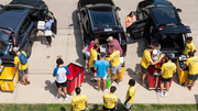 People unloading cars, wearing yellow shirts, outdoor setting.