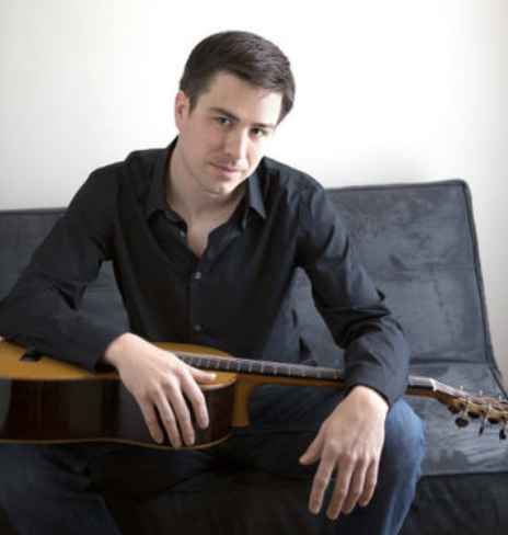 UIS faculty member Adam Larison sitting and holding a guitar