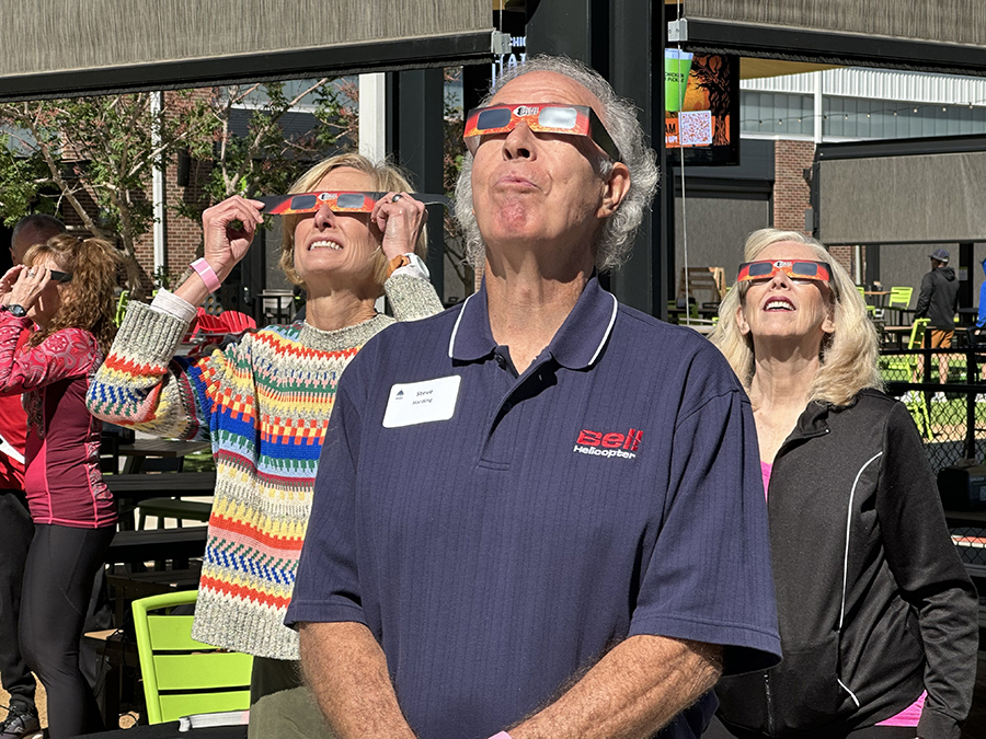 Three individuals watch a solar eclipse with viewing glasses on