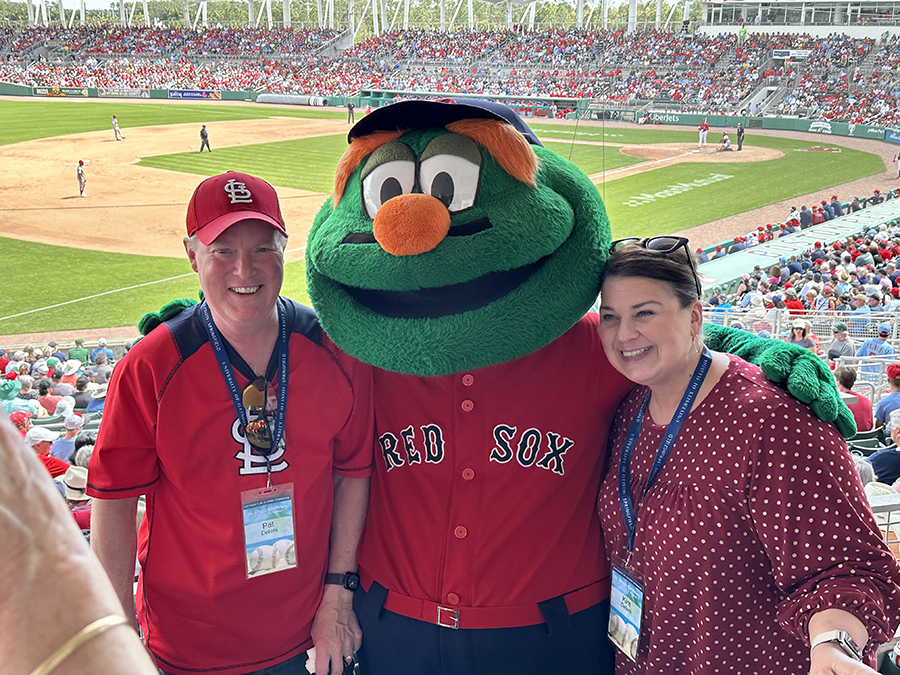 A man and woman pose with the Boston Red Sox mascot in front of a baseball field