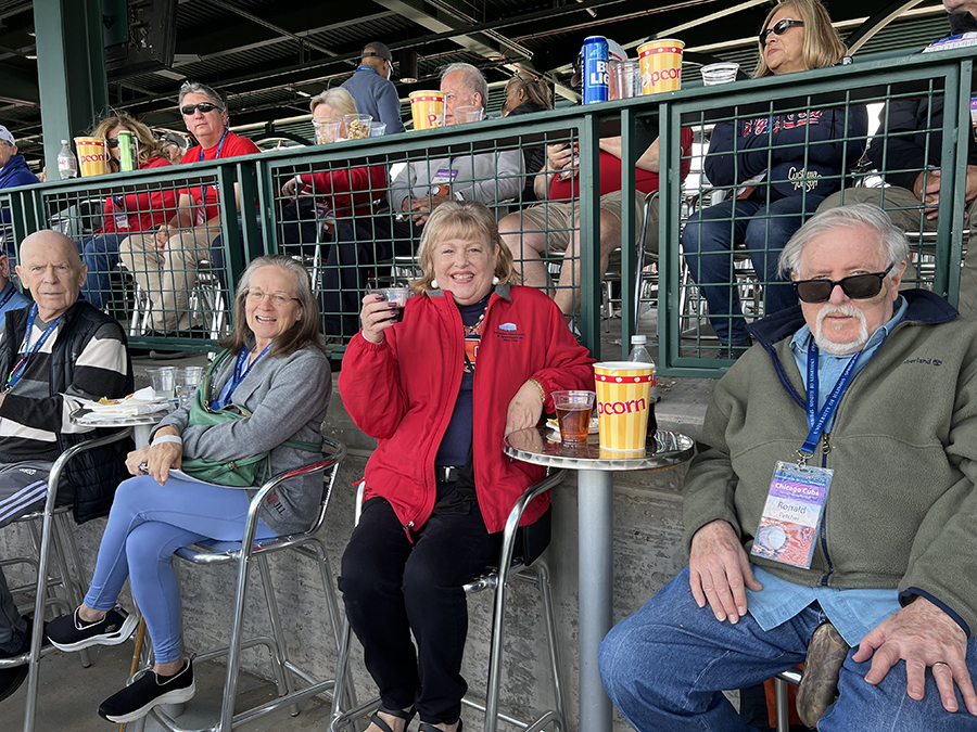 a group of people smile for a picture as they sit in their seats watching a baseball game