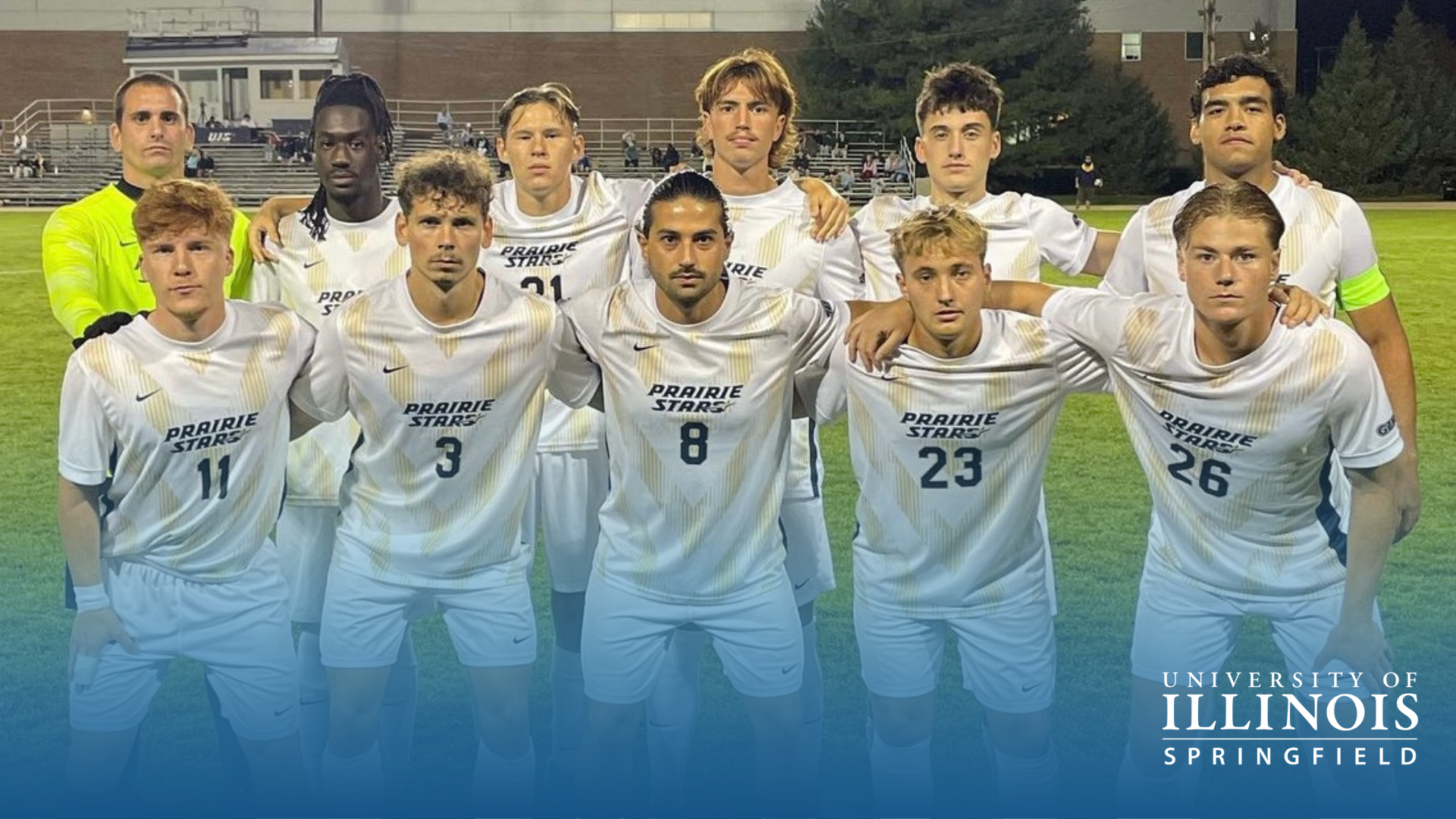 Soccer team posing in white uniforms on a field at night.