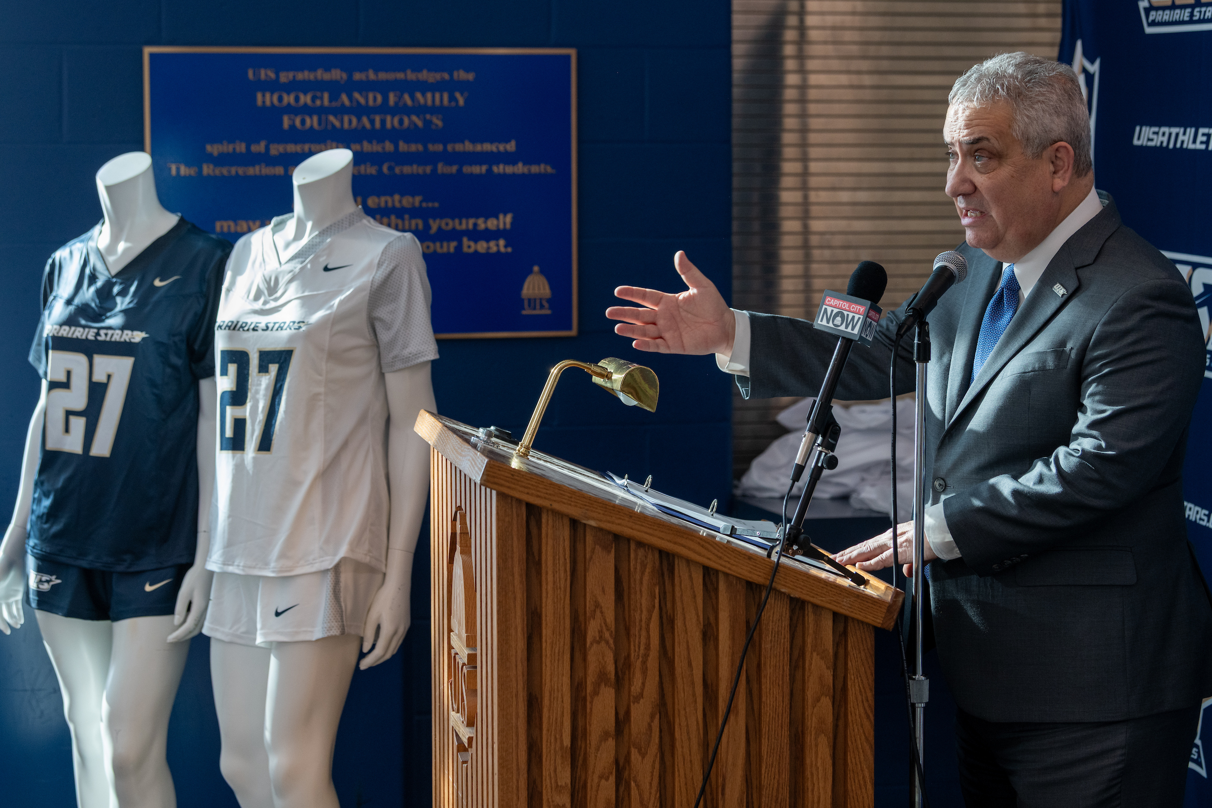 UIS Athletic Director speaks at podium next to mannequins wearing flag football uniforms.