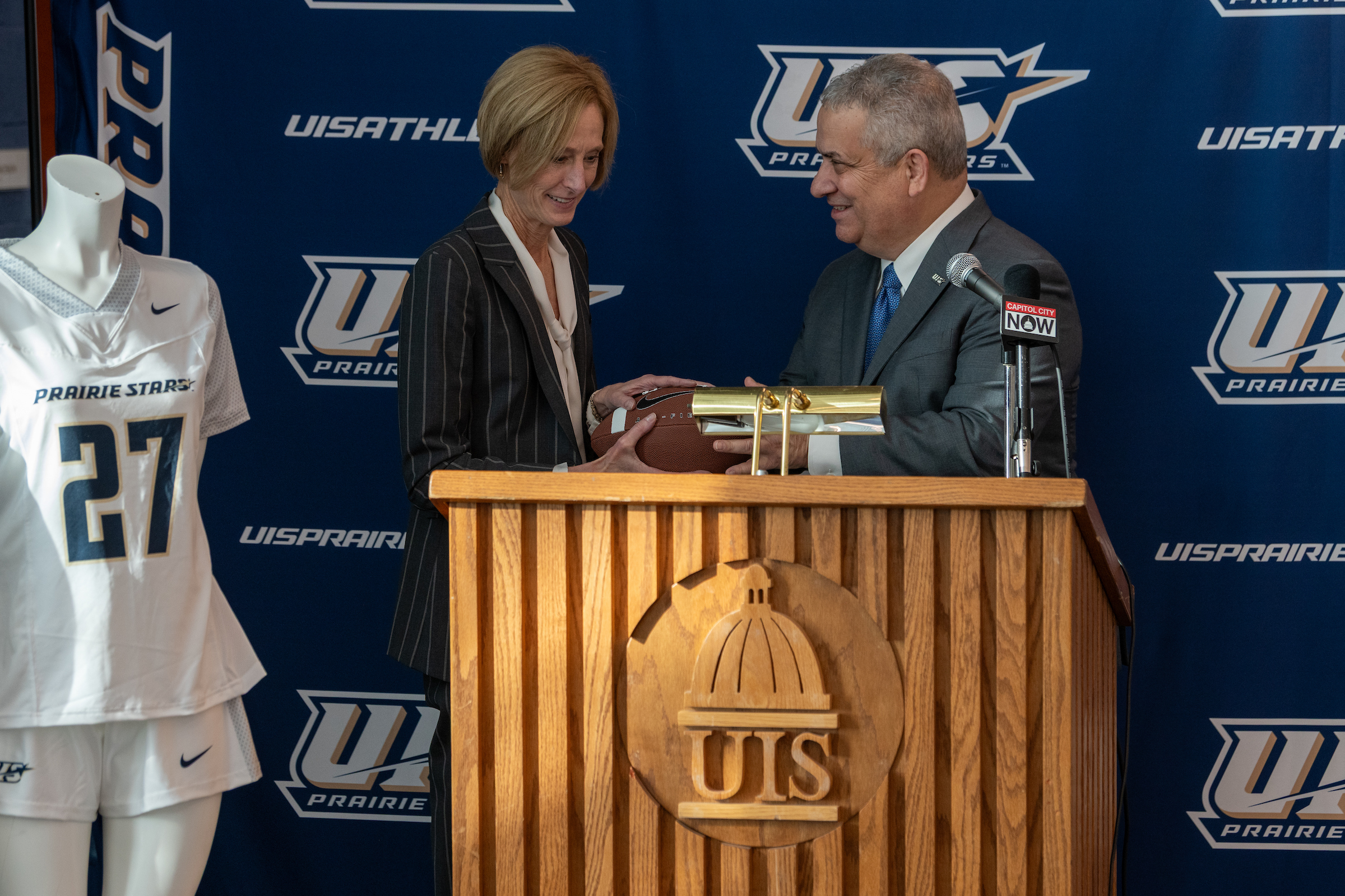 UIS Chancellor Janet Gooch and Athletic Director Mike Herman pose behind a podium with a football.
