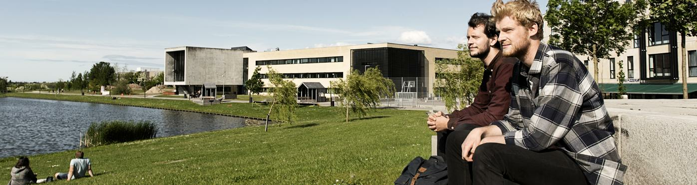 Two male students on-campus looking past green grass and lake