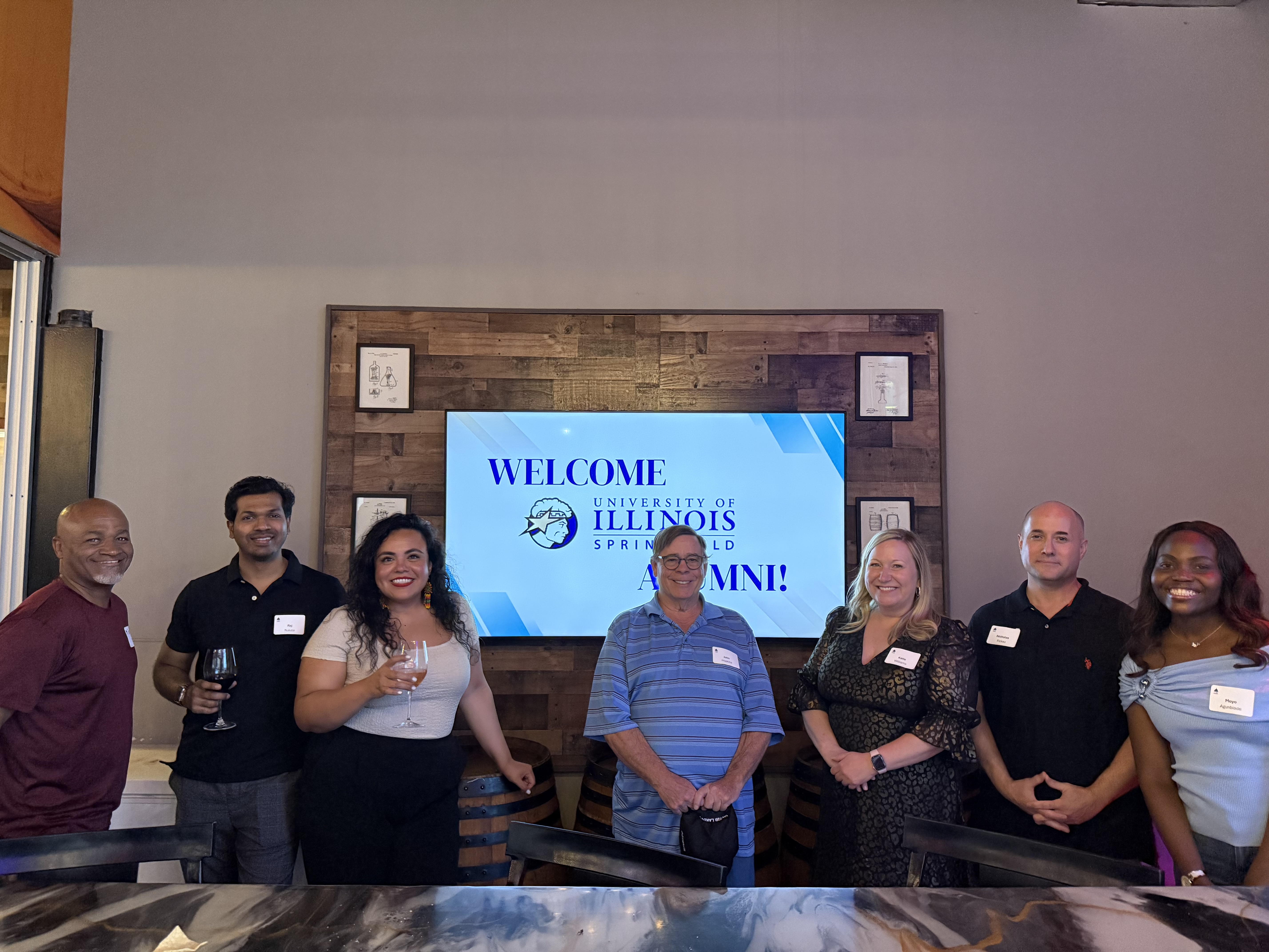 Seven people standing in front of a TV displaying a welcome message.