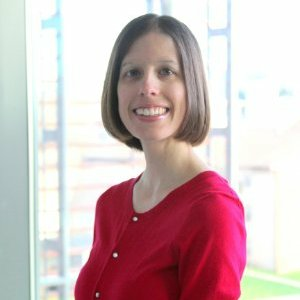 Brooke Newell in a red sweater stands by a window.