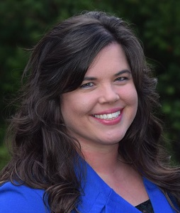 Smiling woman in a blue blouse against a dark background.
