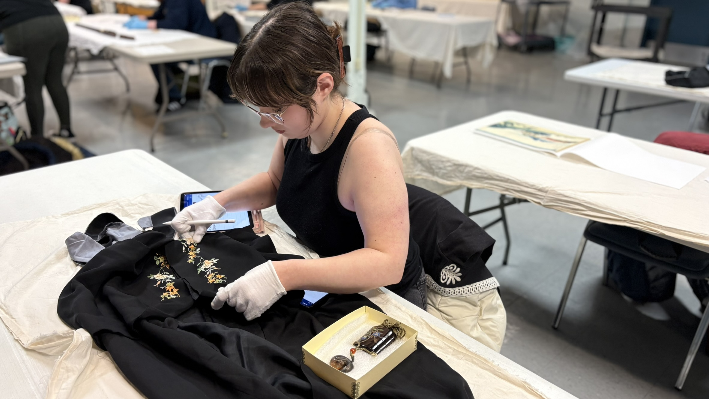 A person wearing gloves sitting at a table with a embroidered black garment