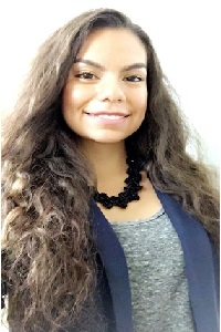 Smiling woman with long curly hair, wearing a necklace and blazer.