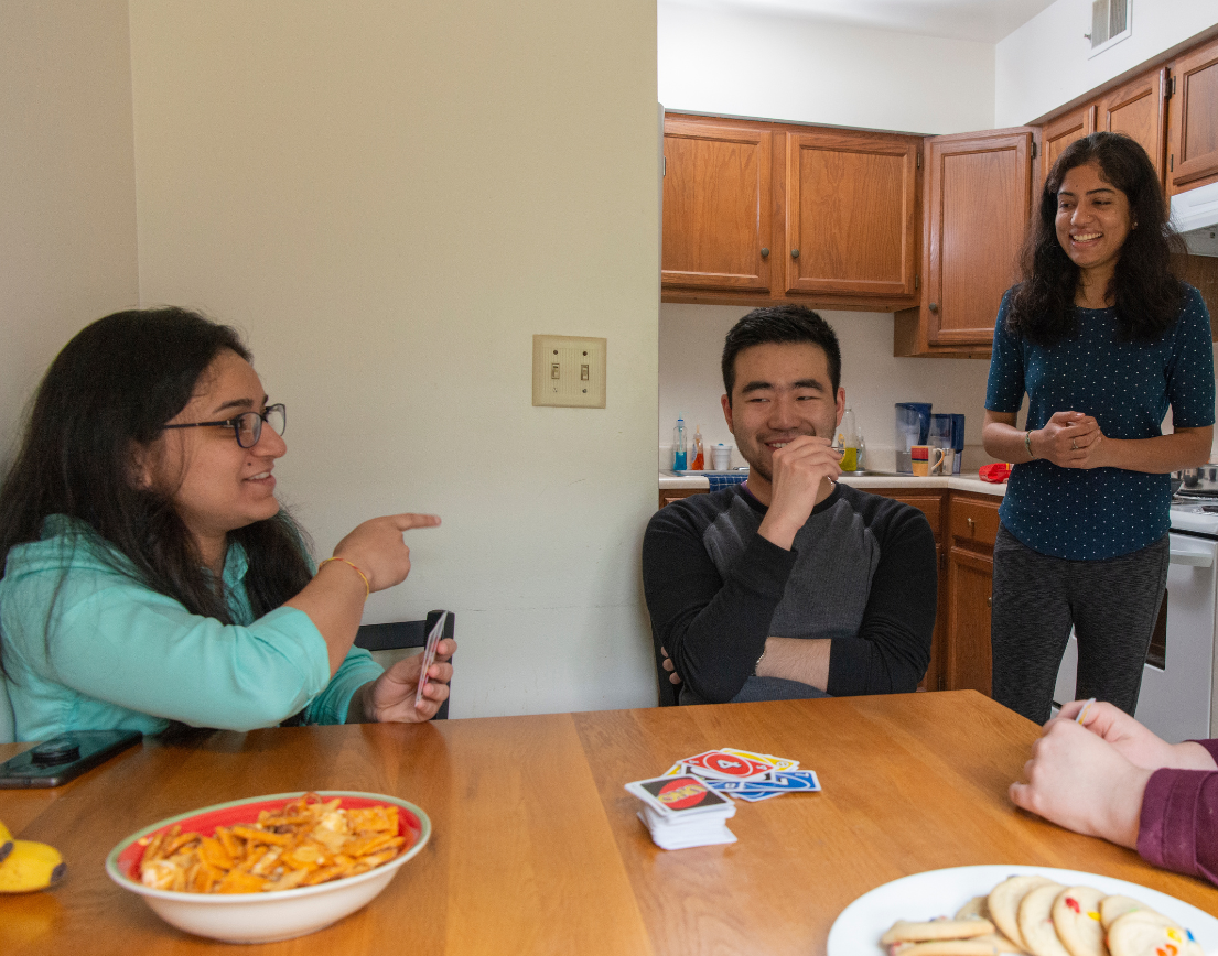 Four friends laughing around a table playing Uno.