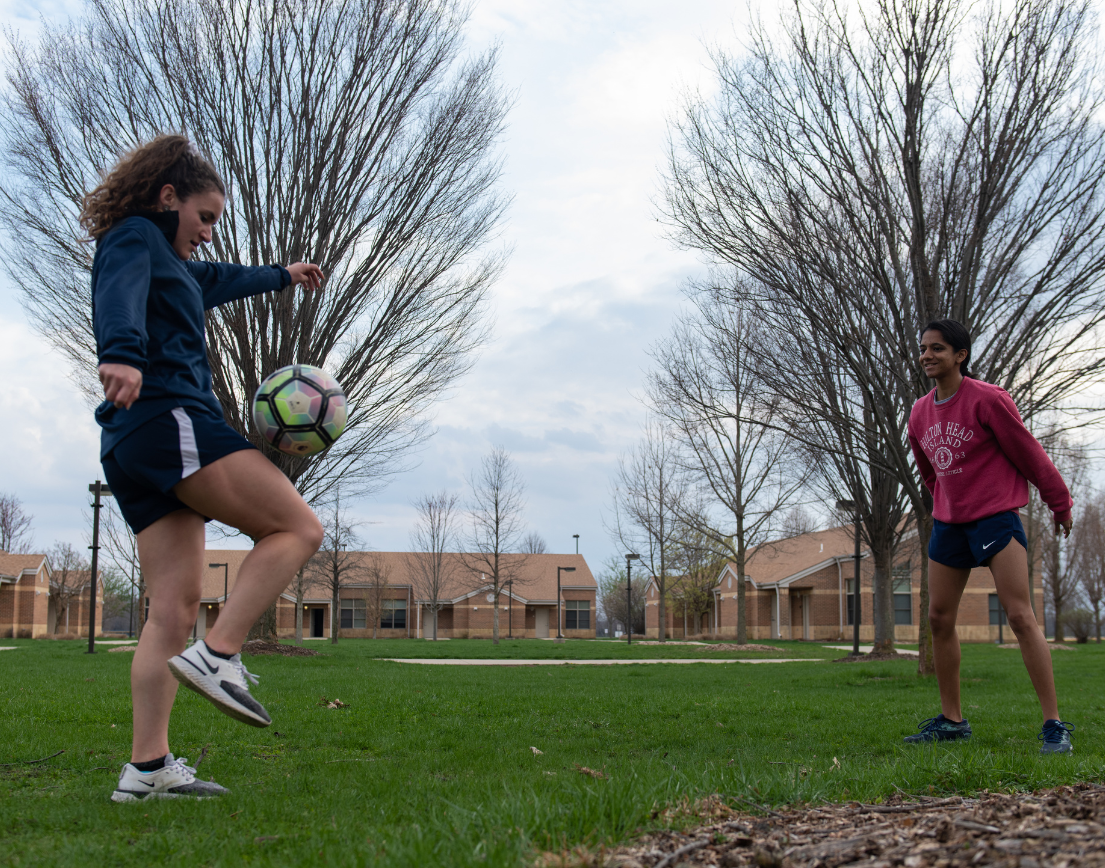 Two girls playing soccer on a green lawn.