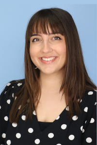 Smiling woman with straight hair and polka dot blouse, blue background.