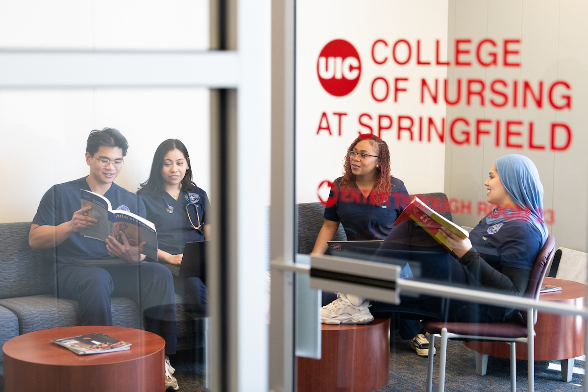 Students in navy scrubs sit and read together in a lounge. The window reads "UIC College of Nursing at Springfield," creating a focused and collaborative mood.
