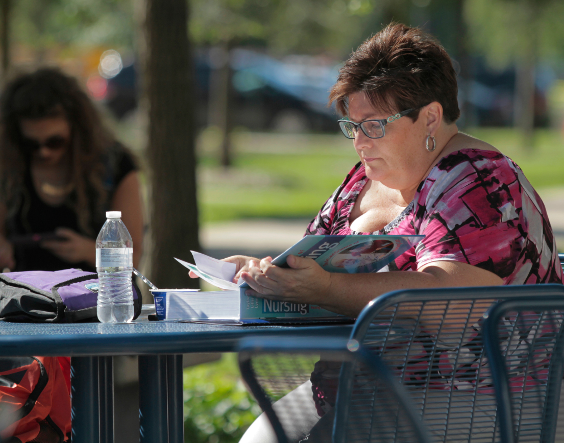 A women reading a book outside at a table.