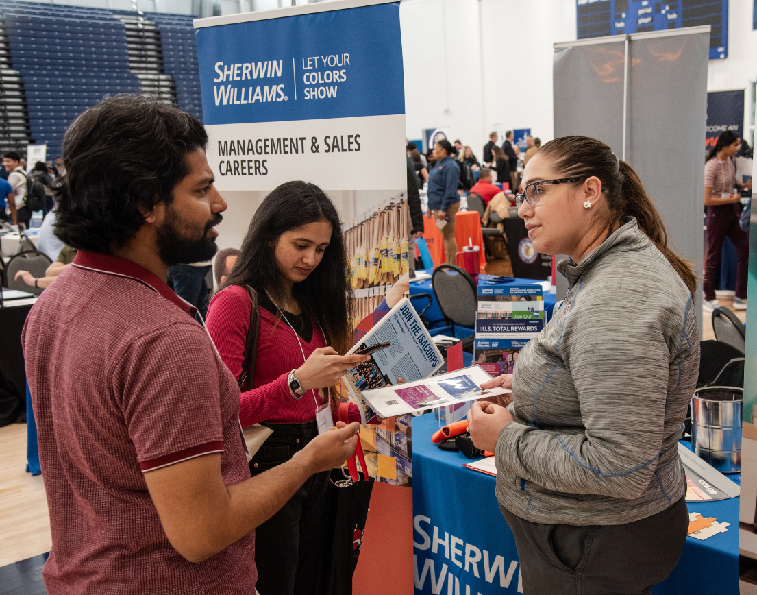 Two students stop to listen to a recruiter at a career fair.