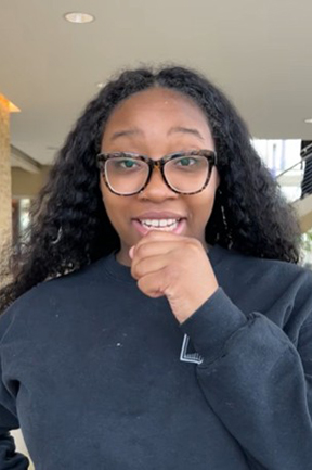 Smiling person with glasses indoors, wearing a black sweater.