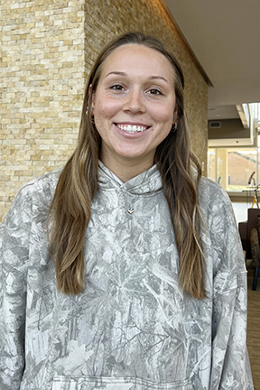 Smiling person in a gray patterned sweatshirt indoors.