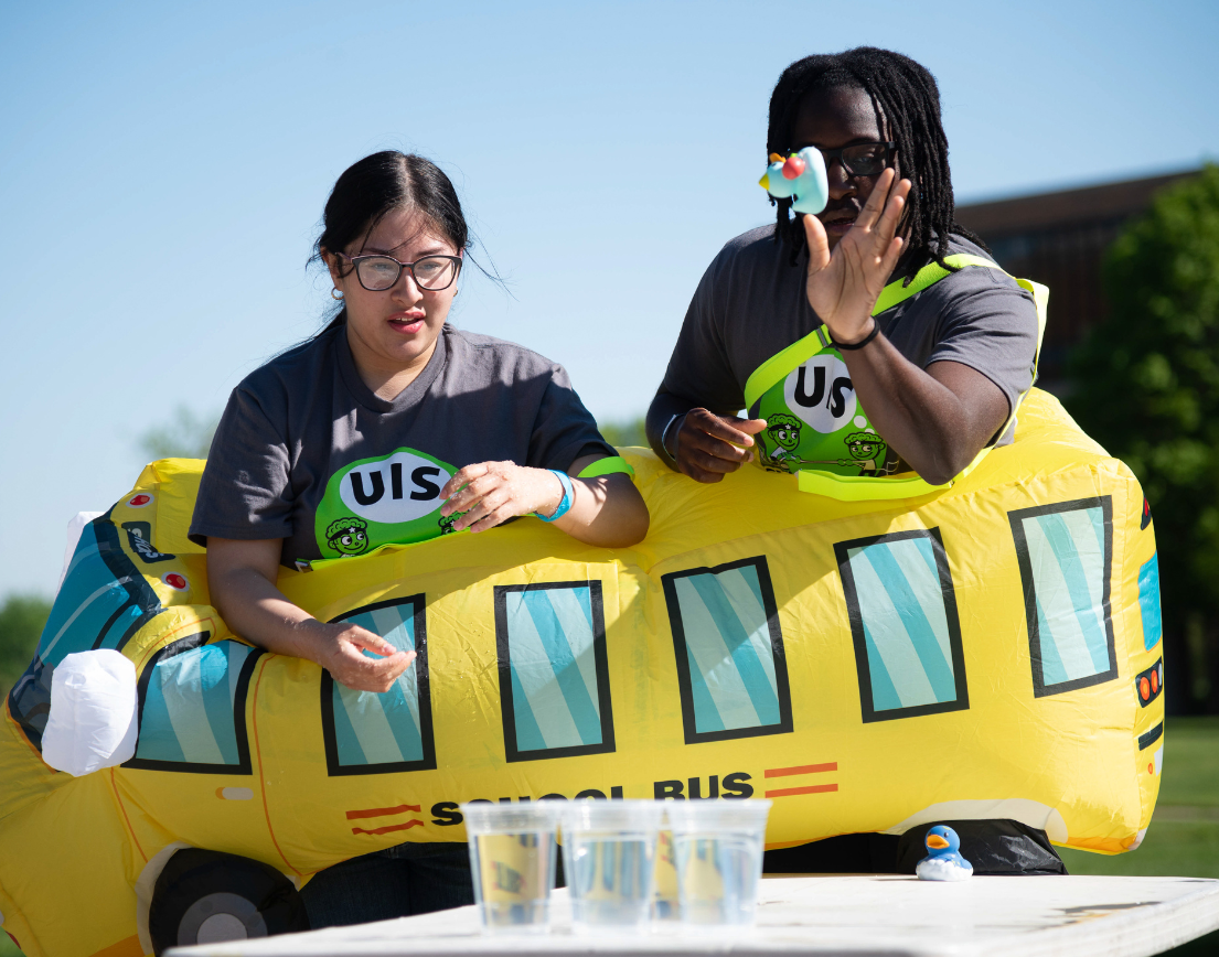 Two students dressed as a bus trying to throw a duck into a cup.