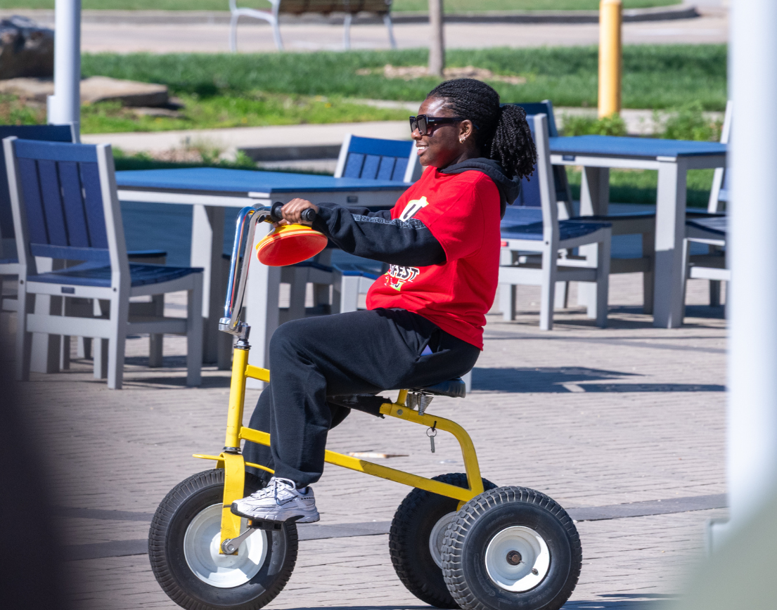 A student in a red shirt rides happily on a tricycle.