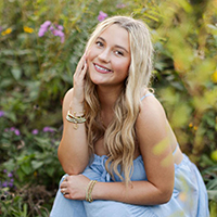 Young woman smiling in a field of wildflowers, wearing a blue dress.